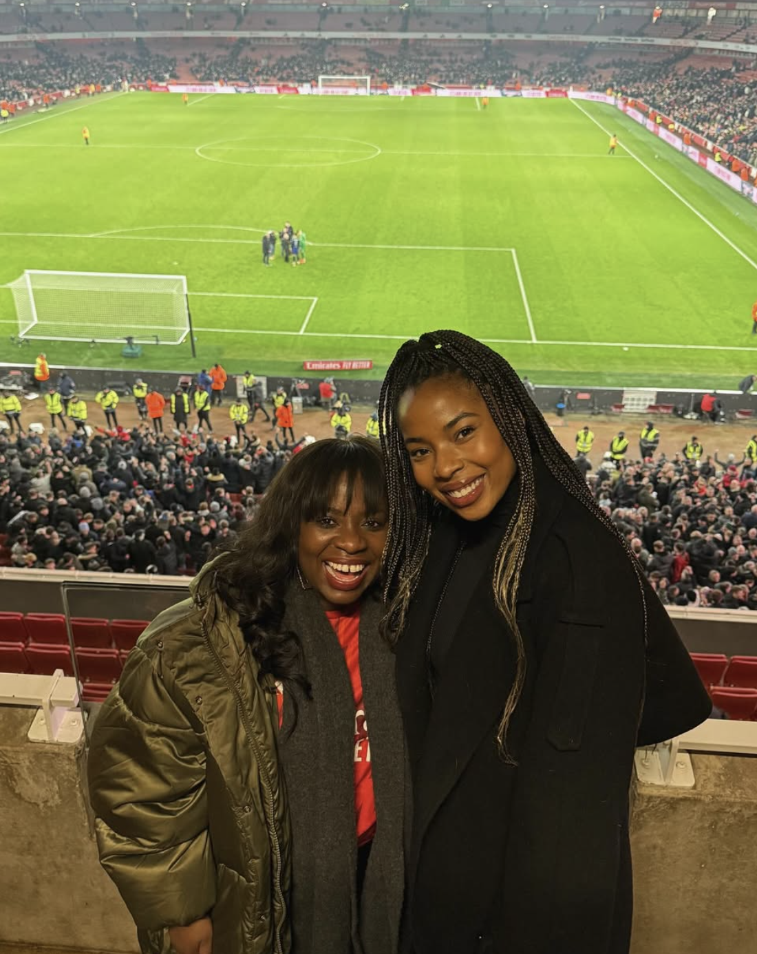 Two Black women smiling in front of soccer field